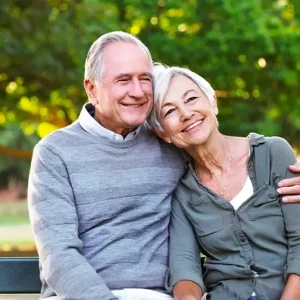 A happy elderly couple sitting on a bench in a park, with the man embracing the woman.