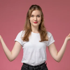 Person wearing a white T-shirt and black jeans meditating with hands in a mudra pose against a pink background.